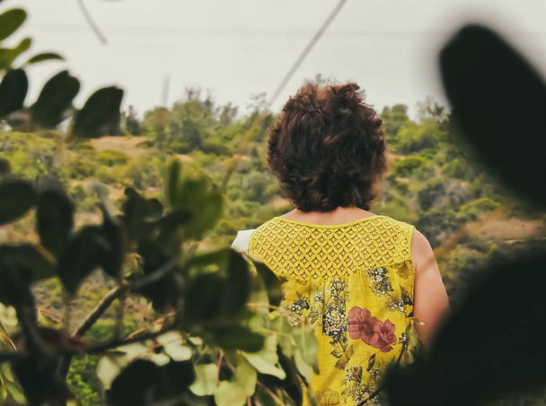 Frau mit gelber Bluse von hinten gesehen zwischen Zweigen - Foto, Bild