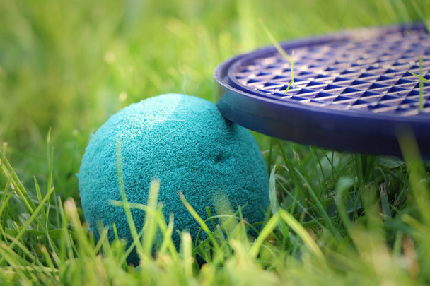 Venkovní aktivity. jemný tenisový zelený míč a měkký randál leží v trávě. Detail pro dětské sportovní vybavení. Modrá a zelená koule a černý randál - Fotografie, Obrázek
