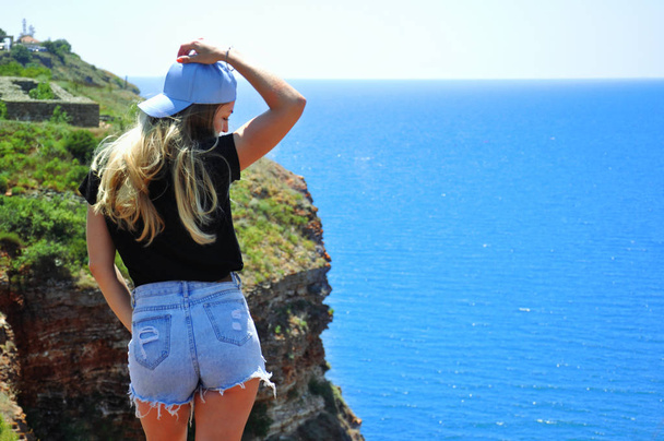 A young girl in denim shorts admires the beautiful scenery. Beautiful girl looks at the sea. - Fotoğraf, Görsel