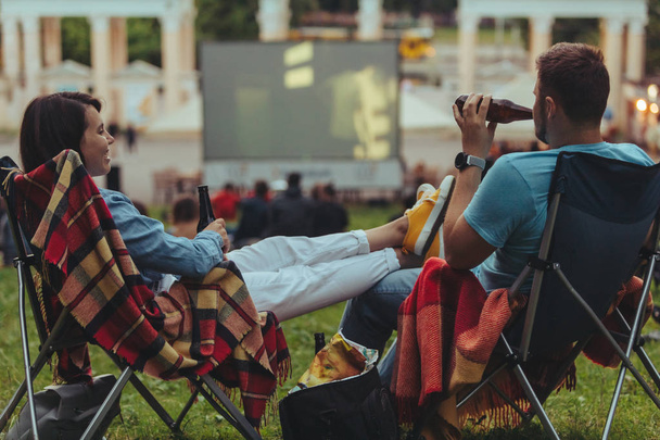 屋外映画館で屋外で映画を見て、都市公園のキャンプチェアに座っているカップル - 写真・画像