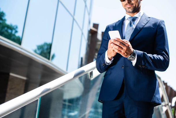 cropped view of man in suit using smartphone outside - Foto, Imagen