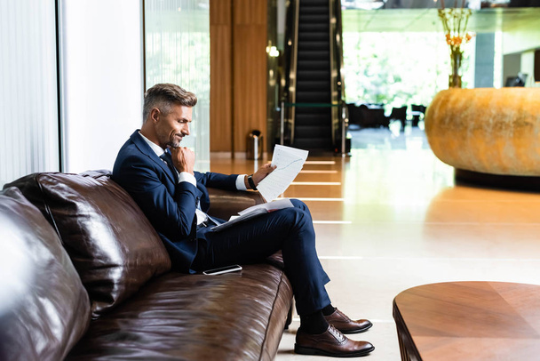 side view of handsome businessman in suit looking at papers  - Foto, Bild