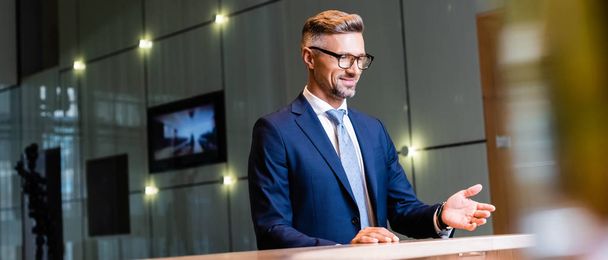 Panoramaaufnahme eines gutaussehenden Geschäftsmannes in Anzug und Brille, der lächelt und wegschaut  - Foto, Bild
