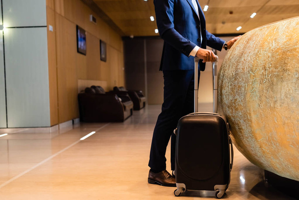 cropped view of businessman in suit holding suitcase in hotel  - Фото, изображение