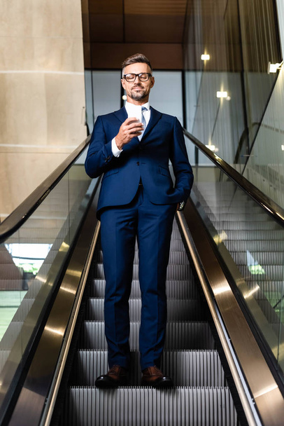 handsome businessman in suit and glasses with hand in pocket using smartphone  - Valokuva, kuva