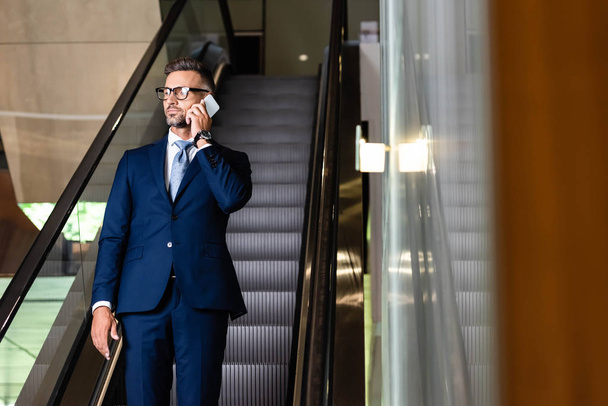 handsome businessman in suit and glasses talking on smartphone  - Zdjęcie, obraz