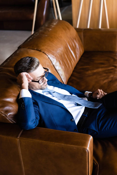high angle view of handsome businessman in suit and glasses sitting on sofa  - Foto, Bild