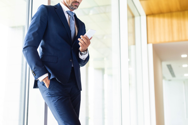 cropped view of businessman in suit with hand in pocket using smartphone  - Foto, imagen