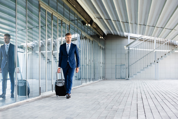 hombre de negocios guapo y confiado en ropa formal que sostiene la maleta
  - Foto, Imagen