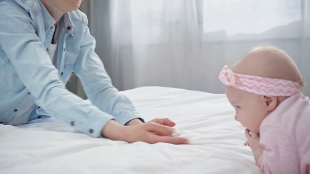Rack focus van gelukkige moeder gebaren in de buurt van zuigeling op bed  - Video