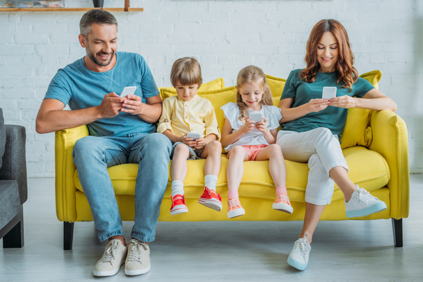 happy mother and father with children sitting on sofa and using smartphones - Foto, immagini