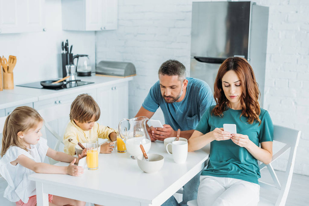 family using smartphones while sitting at kitchen table near served breakfast - Photo, Image