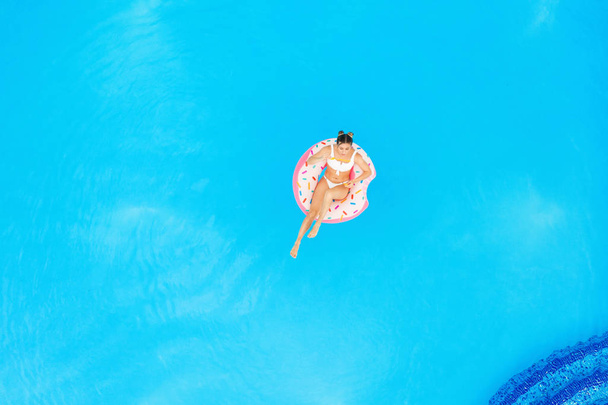 Aerial view of young beautiful girl in a white  bikini relaxing on inflatable donut in the pool. Summer Vacation - Foto, afbeelding