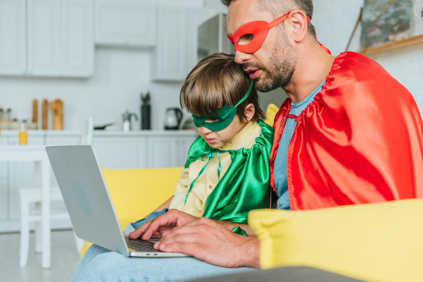 enfoque selectivo de papá e hijo en trajes de superhéroes utilizando el ordenador portátil en casa
 - Foto, Imagen