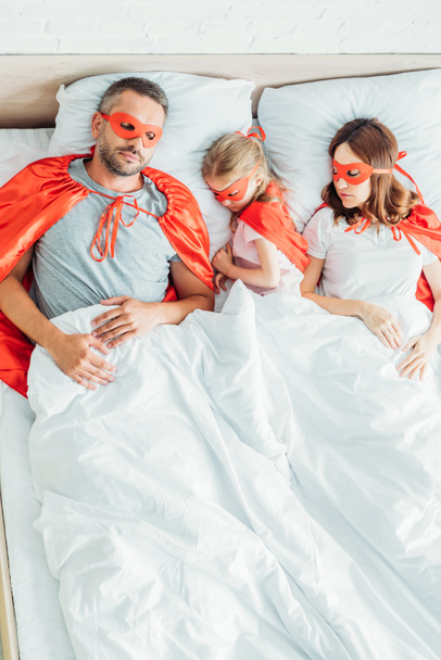 top view of family sleeping on white bedding in costumes of superheroes  - Foto, afbeelding