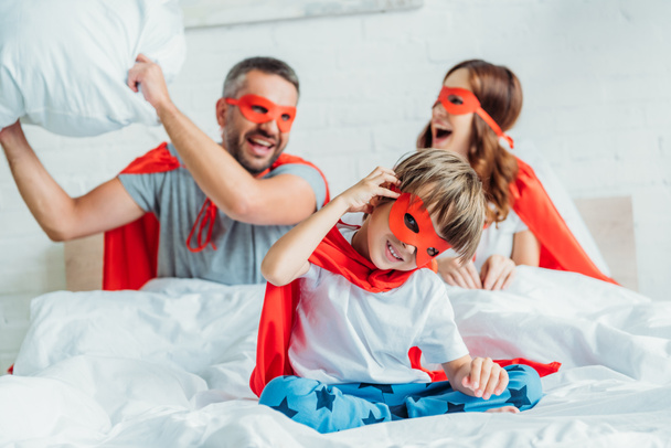ευτυχισμένη οικογένεια σε κοστούμια των υπερήρωες αγωνίζονται με μαξιλάρι στο κρεβάτι  - Φωτογραφία, εικόνα