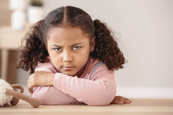 Triste niña afroamericana sentada a la mesa
 - Foto, imagen