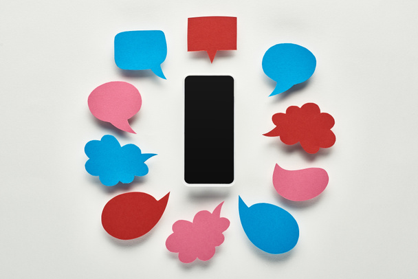 vista superior do smartphone com tela em branco no fundo branco perto de bolhas de fala coloridas vazias, conceito de cyberbullying
 - Foto, Imagem