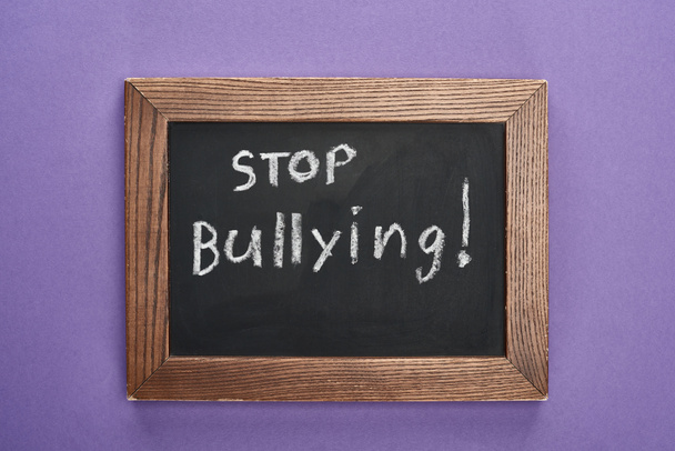 Top uitzicht op schoolbord in houten frame met stop pesten belettering op paarse achtergrond - Foto, afbeelding