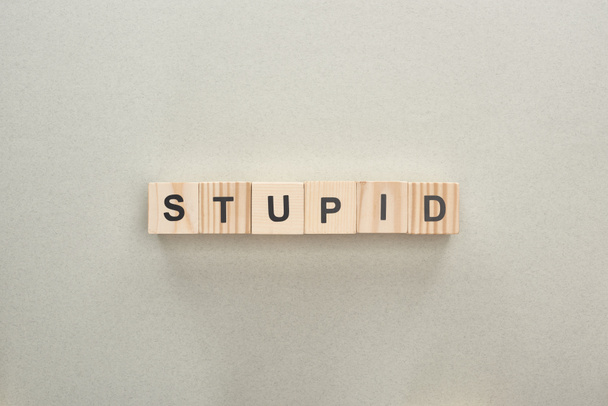 top view of wooden blocks with stupid lettering on grey background, bullying concept - Photo, Image