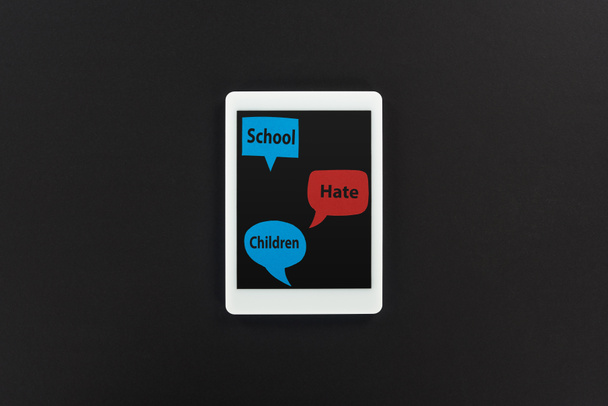 felülnézet a digitális tabletta és a beszéd buborékok az iskola, a gyűlölet és a gyermekek szavait a fekete háttér, online zaklatás koncepció - Fotó, kép