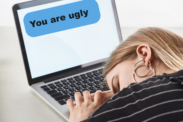 szőke lány alszik közelében laptop veled csúnya üzenet a képernyőn, cyberbullying koncepció - Fotó, kép