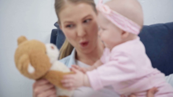 mother holding teddy bear near infant daughter  - Felvétel, videó