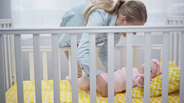Szczęśliwa matka bierze córkę leżącą w łóżeczku dziecięcej  - Materiał filmowy, wideo