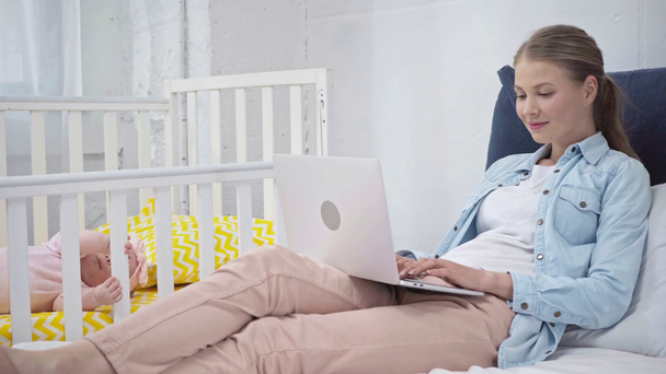mother typing on laptop near daughter in baby crib  - Кадри, відео