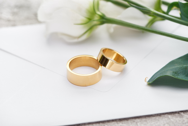 golden wedding rings on white envelope near white flowers - 写真・画像