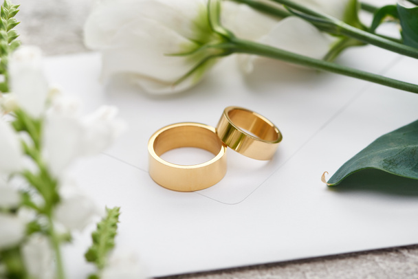 selective focus of wedding rings on white envelope near white eustoma flowers - Фото, изображение