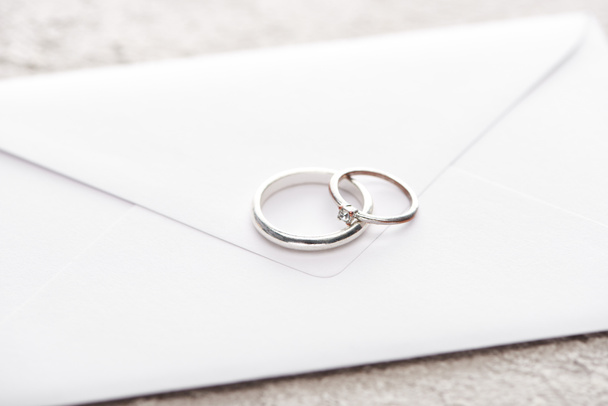 silver wedding rings on white envelope on grey textured surface  - Foto, Imagem