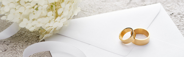 panoráma szemcsésedik-ból arany gyűrű-ra boríték mellett fehér szalag és Hortense virág-ra szürke szövet felszín - Fotó, kép