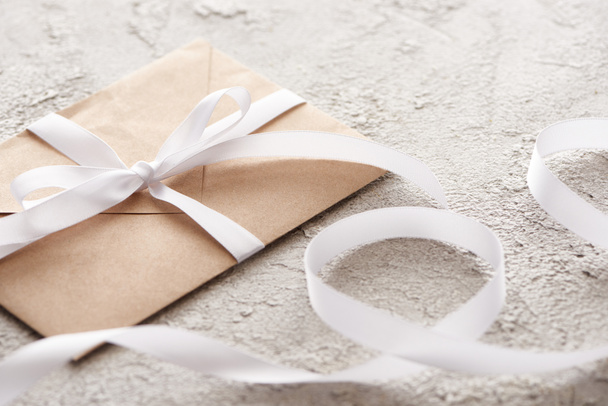 foyer sélectif de l'enveloppe beige avec ruban blanc sur surface grise texturée
  - Photo, image