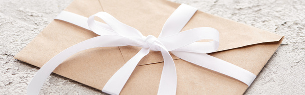 panoramic shot of beige envelope with white ribbon on textured surface - 写真・画像