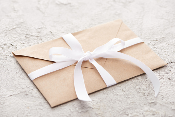 beige envelope with white ribbon on grey textured surface - Photo, Image