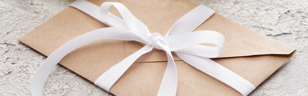 panoramic shot of beige paper envelope with white ribbon on textured surface - Фото, зображення
