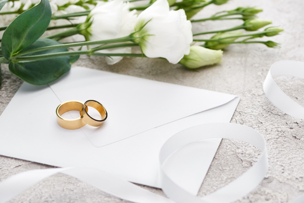 golden wedding rings on white envelope near eustoma flowers and white ribbon - Photo, Image