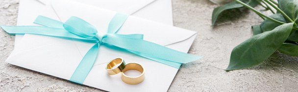 panoramic shot of golden rings on white envelopes with blue ribbon on textured surface - Photo, Image
