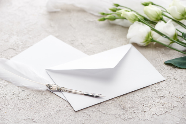 white envelope near eustoma flowers and quill pen on grey textured surface   - Photo, Image