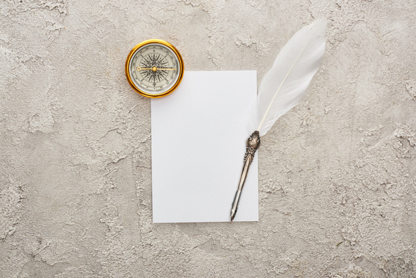 top view of quill pen on white card near golden compass on grey textured surface - Fotoğraf, Görsel