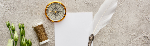 πανοραμική φωτογραφία πένας σε λευκή κάρτα κοντά σε χρυσή πυξίδα, καρούλι και λευκά άνθη ευστόμα σε γκρίζα υφή - Φωτογραφία, εικόνα