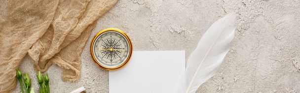 Colpo panoramico di penna d'oca su pezzo di carta vicino sacco beige e bussola dorata su superficie grigia testurizzata
 - Foto, immagini