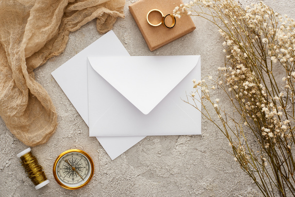 top view of envelope near beige sackcloth, golden compass and wedding rings on textured surface - Photo, Image