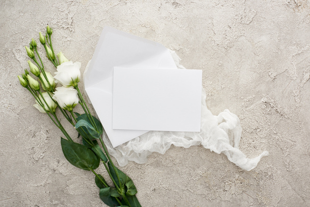top view of blank white card on white cheesecloth near eustoma flowers on textured surface - Photo, Image