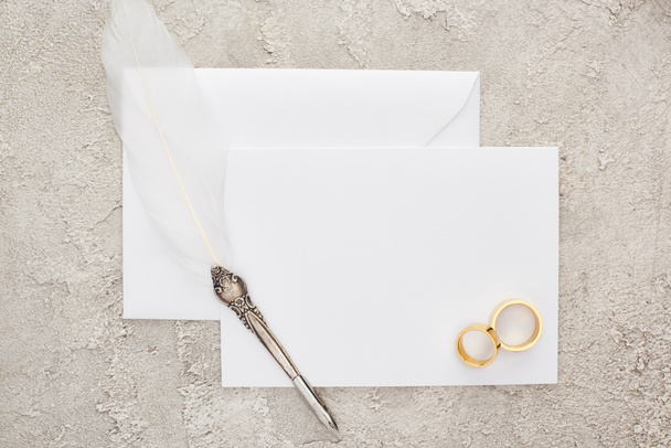 felülnézet az esküvő gyűrűk és tollszár toll fehér üres kártya textúrájú felület  - Fotó, kép