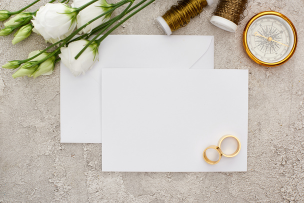 vista superior de anéis dourados no cartão vazio perto de flores eustoma, bobbins e bússola dourada na superfície cinza
 - Foto, Imagem