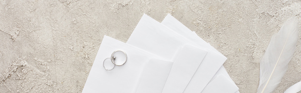 panoramic shot of silver rings on white envelopes on textured surface  - Foto, Imagem