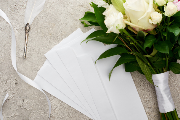 top view of envelopes near bouquet, white ribbon and quill pen on grey textured surface  - Photo, Image