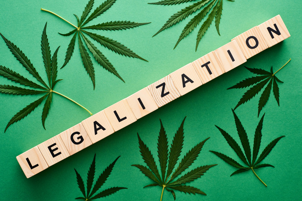 top view of green cannabis leaves and legalization word on wooden blocks on green background - Photo, Image